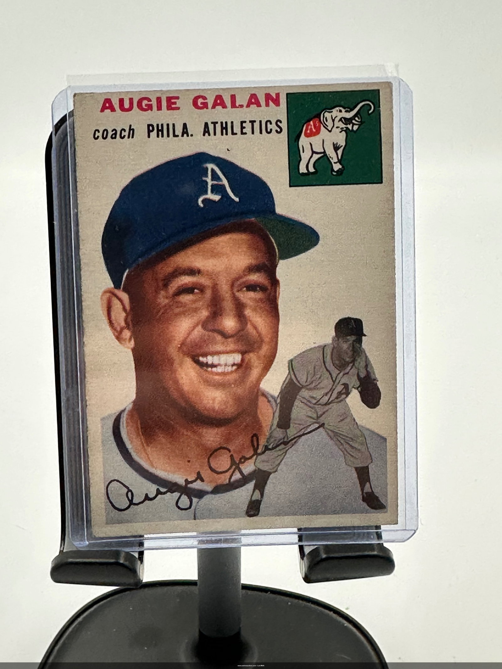 1954 Topps baseball card of Augie Galan,: Vintage 1954 baseball card featuring Augie Galan, a coach for the Philadelphia Athletics. The card prominently displays a smiling portrait of Galan wearing his team cap and includes graphics of the At