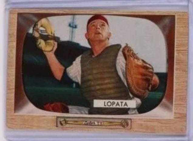 1955 Bowman Stan Lopata Baseball Card: Vintage 1955 Bowman Stan Lopata baseball card featuring the player in his catcher gear, prepared to receive a pitch. The card showcases a classic design with a wooden frame aesthetic and prominently d