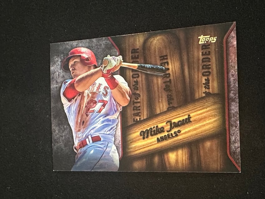 2015 Topps Heart of the Order Mike Trout Baseball Card: This is a 2015 Topps Baseball insert card featuring Los Angeles Angels superstar Mike Trout. It is from the 'Heart of the Order' insert set and showcases a unique design with wooden bat imagery.