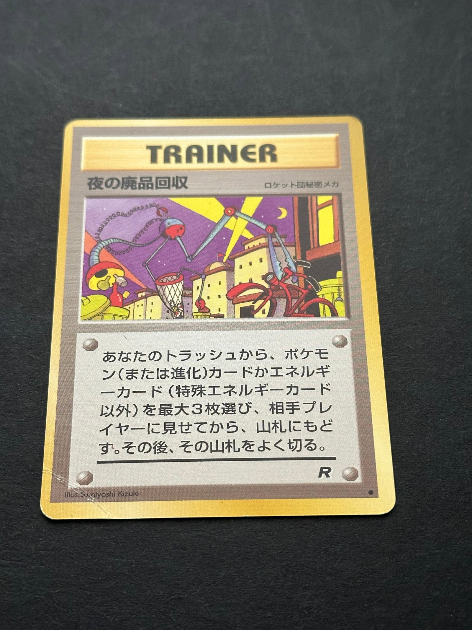 Rocket's Secret Experiment Japanese Pokemon Card: Japanese rocket's secret experiment (yoru no haikibutsu kaishu) trainer card from the team rocket expansion. It is a non-holographic card featuring the iconic team rocket art style. Maybe stickers or