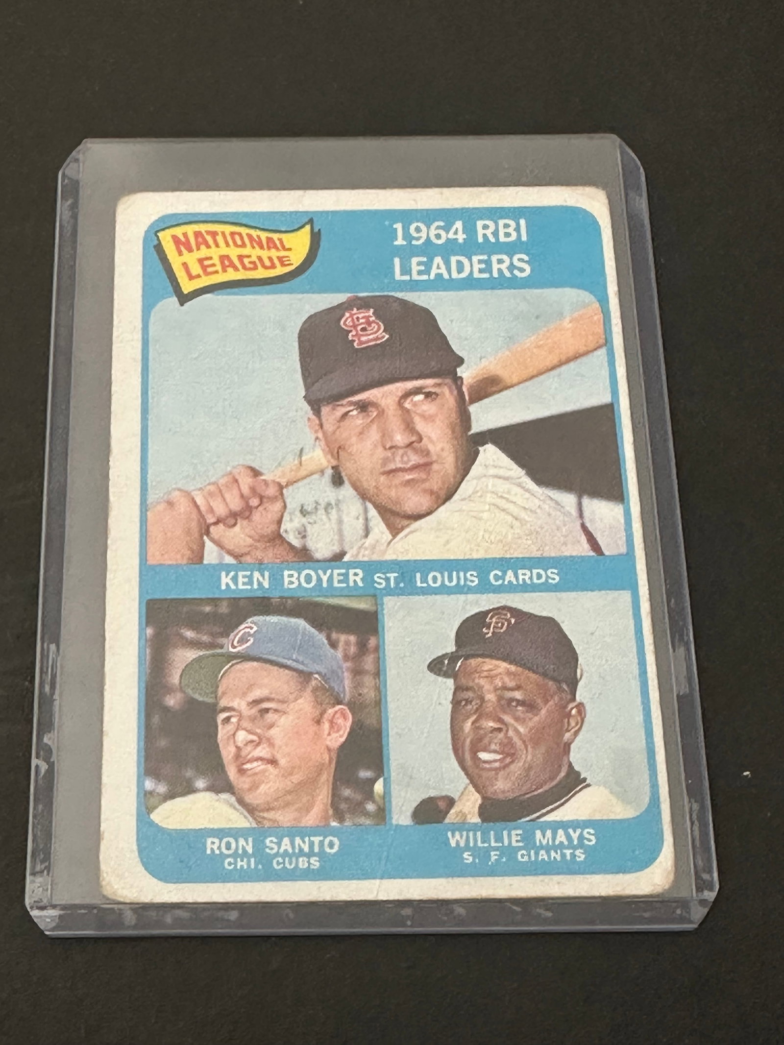 National League R.B.I. Leaders.: This is a 1965 topps baseball card featuring national league rbi leaders ken boyer, willie mays, and ron santo. The card is preserved in a protective hard plastic top-loader case. It shows the three