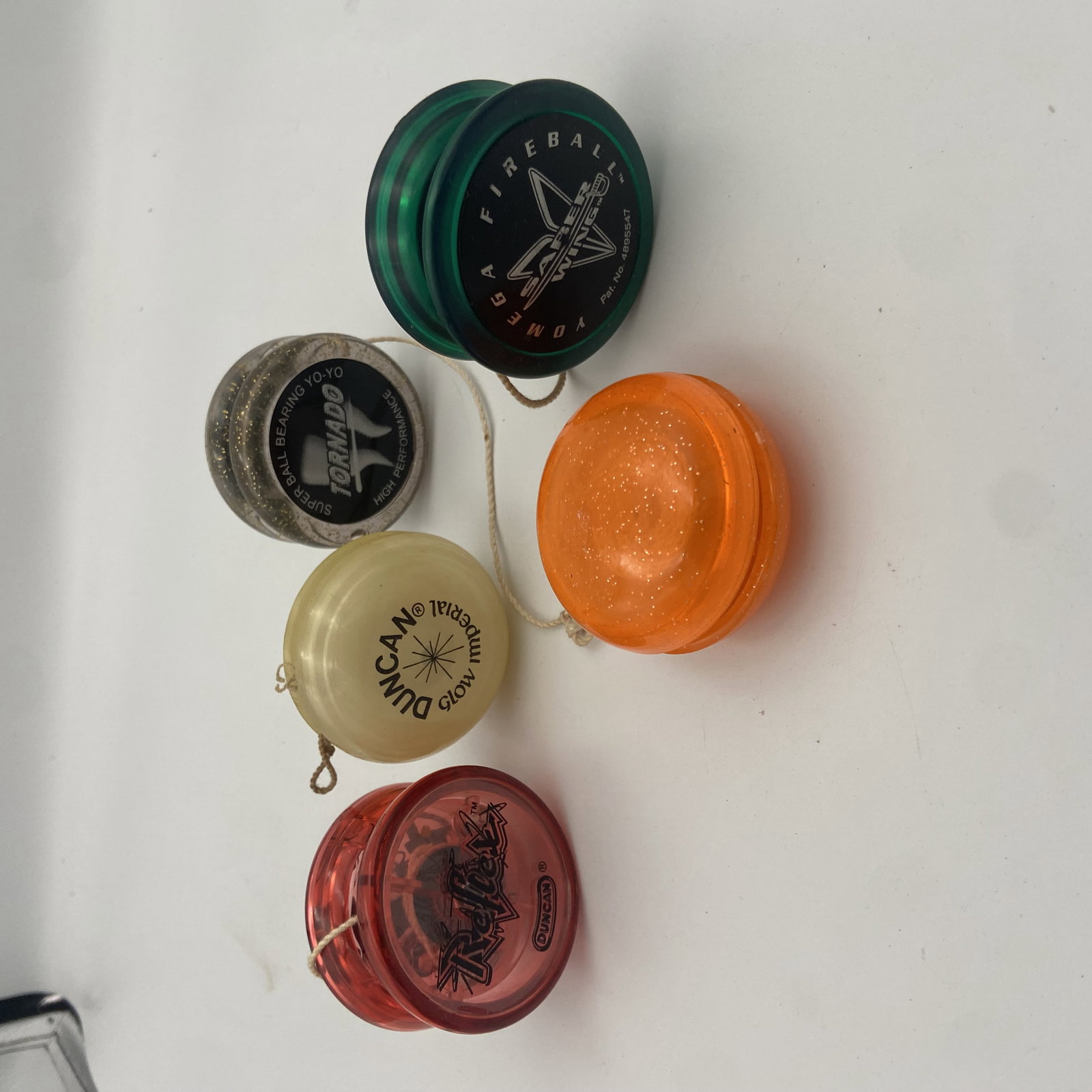 5 Vintage Yo-Yos Yomega and Duncan: collection of five assorted yo-yos including models from Yomega and Duncan. The lot features a green Yomega Fireball, a silver glitter Tornado, an orange glitter yo-yo, a glow-in-the-dark Duncan