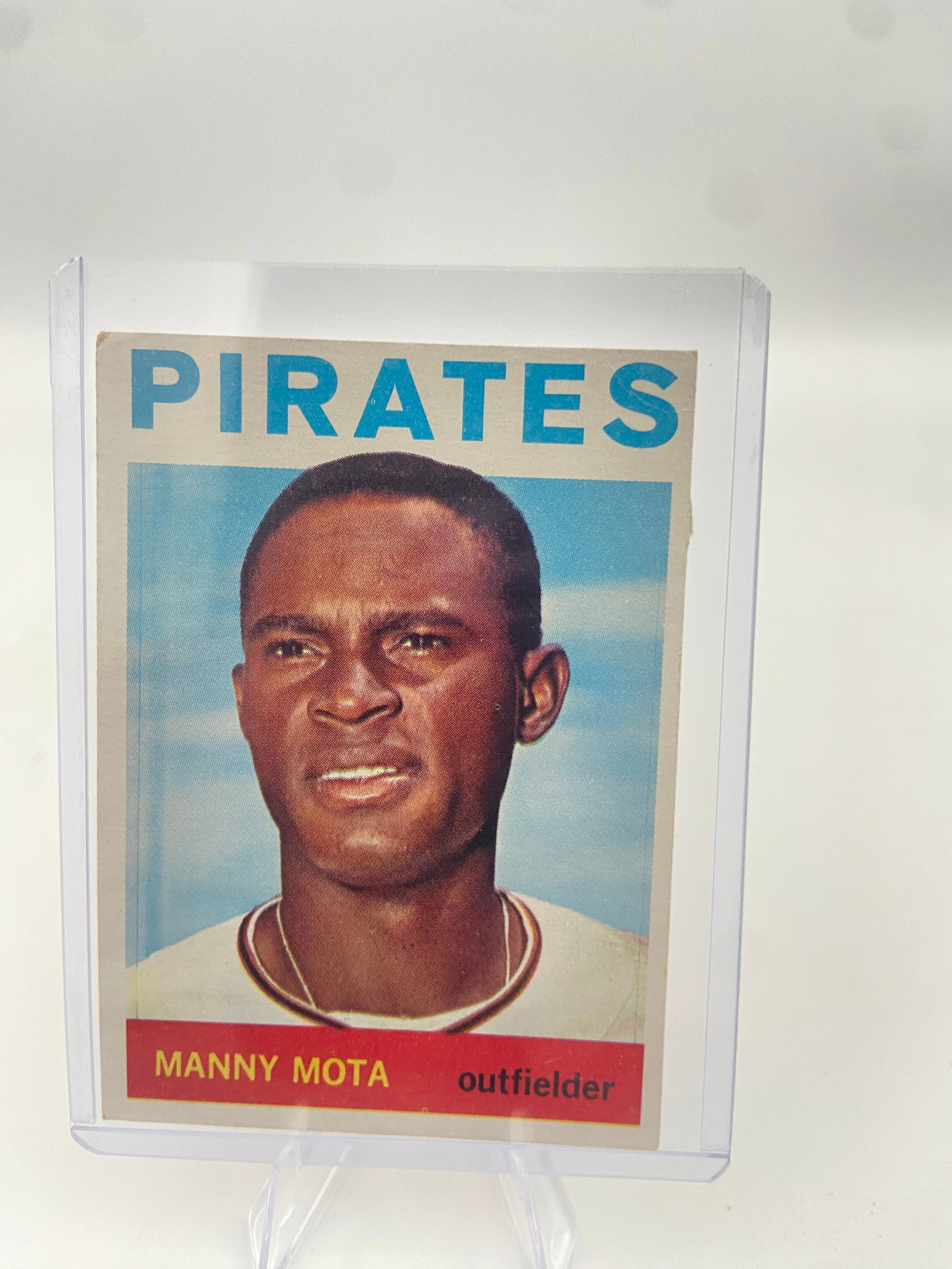 1966 Topps Manny Mota Pittsburgh Pirates Baseball Card: This is a 1966 Topps baseball card featuring Pittsburgh Pirates outfielder Manny Mota. The card is protected in a hard plastic top loader sleeve. It displays a portrait shot of the player with the tea