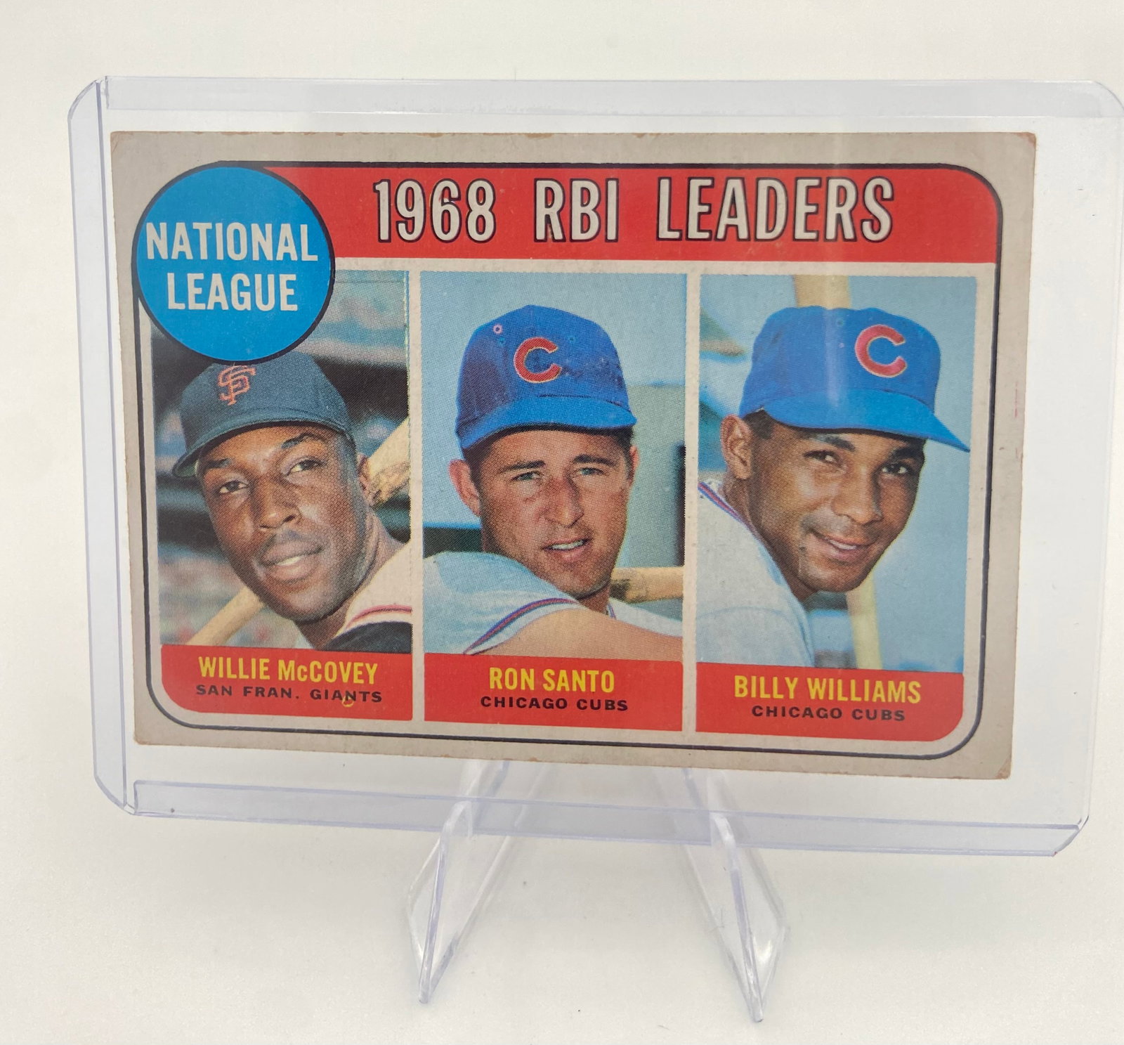 1969 Topps NL RBI Leaders McCovey/Santo/Williams Card: This is a 1969 Topps National League RBI Leaders baseball card featuring Willie McCovey, Ron Santo, and Billy Williams. The card is encased in a protective plastic top loader and shows slight signs