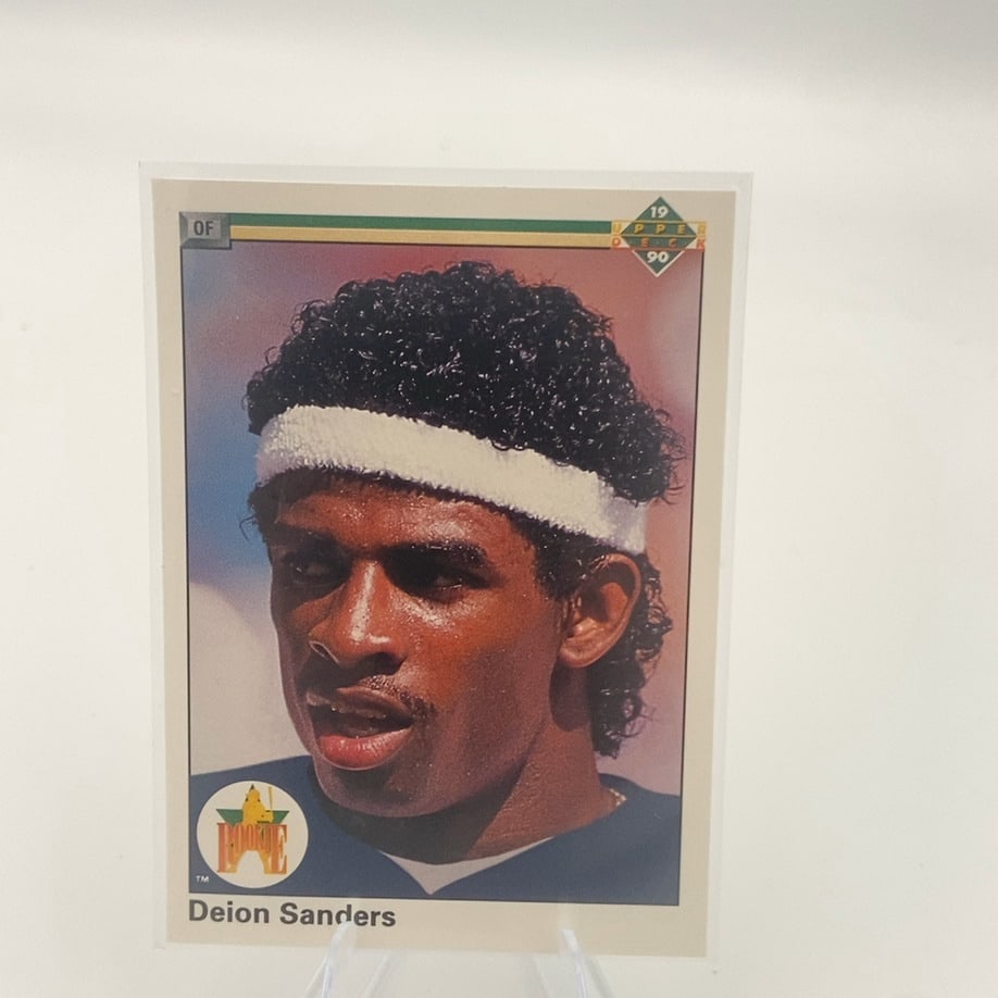 1990 Upper Deck Deion Sanders Rookie Card: This is a 1990 Upper Deck baseball trading card featuring Deion Sanders. The card showcases a classic headshot portrait of the multi-sport athlete during his early career. It is labeled with the 'Rook