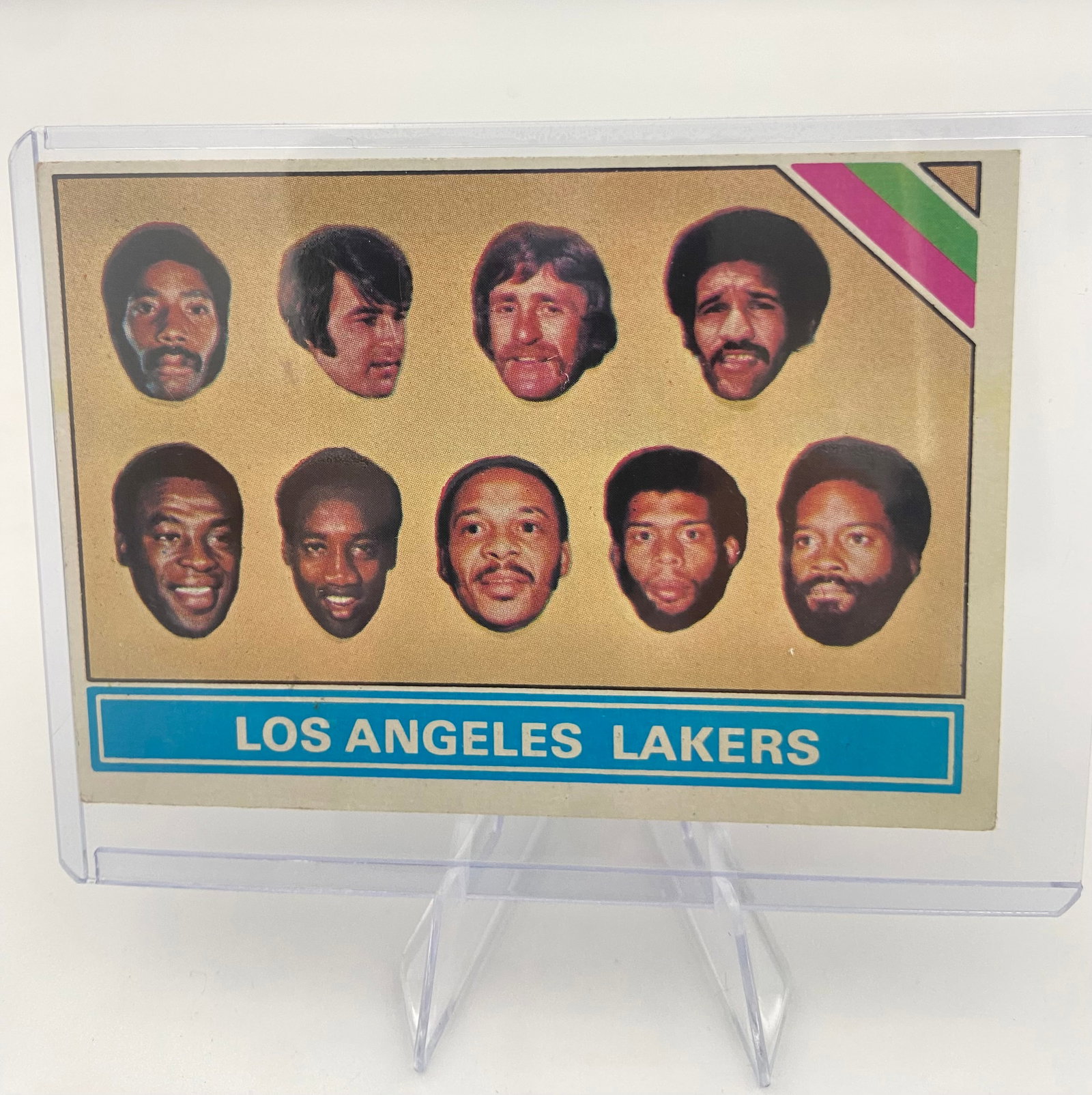 1972-73 Topps Los Angeles Lakers Team Card: This is a 1972-73 Topps Los Angeles Lakers basketball team card featuring portraits of several players from the iconic squad. The card is encased in a protective plastic top loader. It is a classic