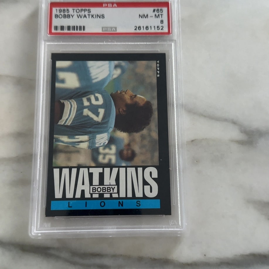 1985 Topps Bobby Watkins: This is a graded 1985 Topps football trading card featuring Bobby Watkins of the Detroit Lions. The card is encased in a protective PSA slab and has been professionally graded as NM-MT 8.