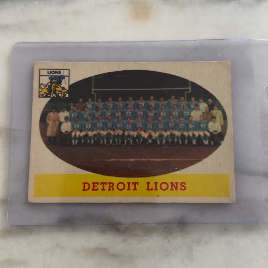 1960 Topps Detroit Lions Team Card: This is a vintage 1960 Topps football trading card featuring a team photo of the Detroit Lions. The image is framed within an oval with the Detroit Lions text printed in red on a yellow bar at the