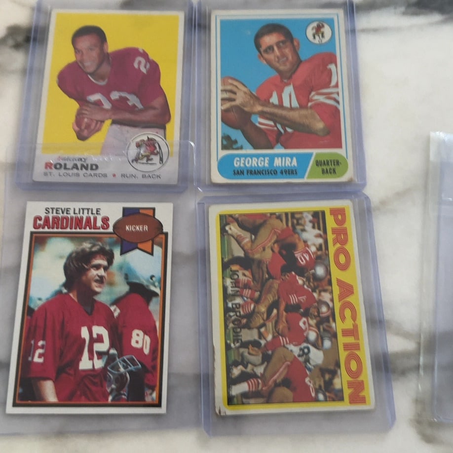 Vintage Football Trading Card Assortment: This lot features four vintage football trading cards encased in protective plastic sleeves. The collection includes cards of Johnny Roland, George Mira, Steve Little, and a John Brodie Pro Action