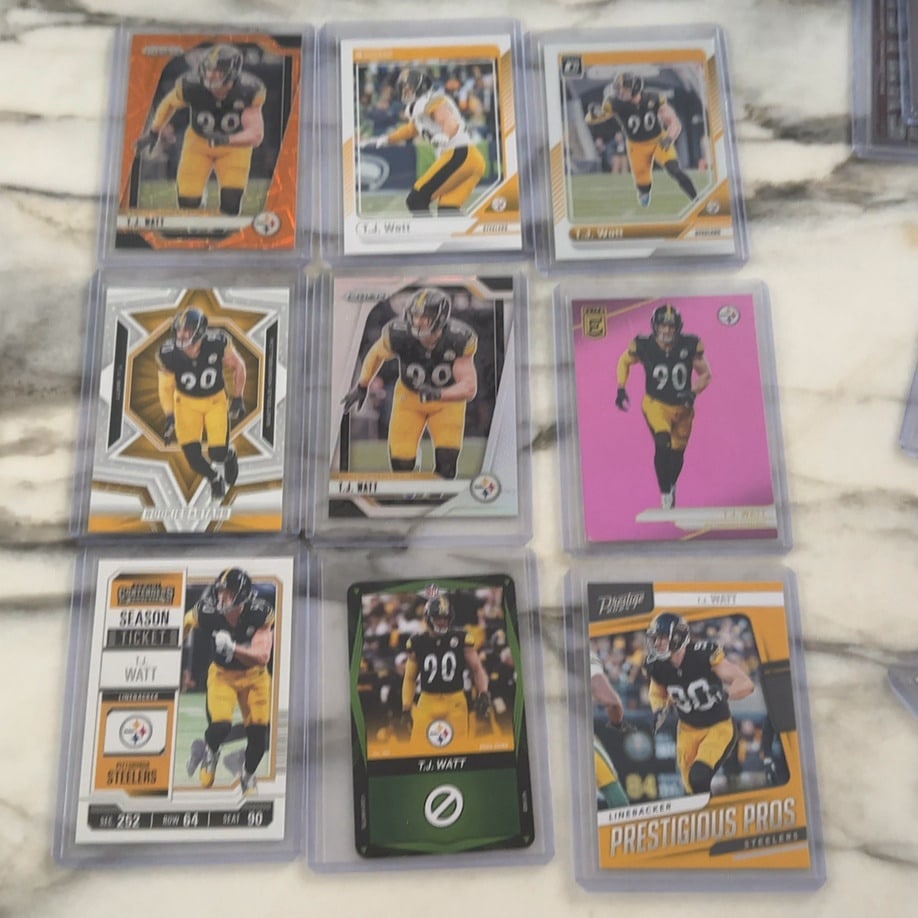 T.J. Watt Football Card Collection: A collection of nine T.J. Watt Pittsburgh Steelers football cards in protective sleeves. The assortment features various Panini brands and designs, including Prizm, Donruss, Optic, Elite, Contenders,
