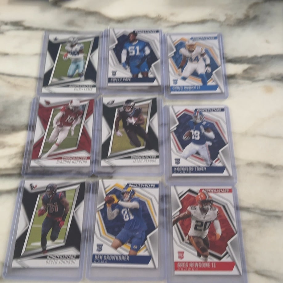 2021 Panini Rookies & Stars Football Card Collection: A collection of nine 2021 Panini Rookies & Stars football cards housed in individual plastic top-loaders. The set features various professional football players, including rookies identified by the
