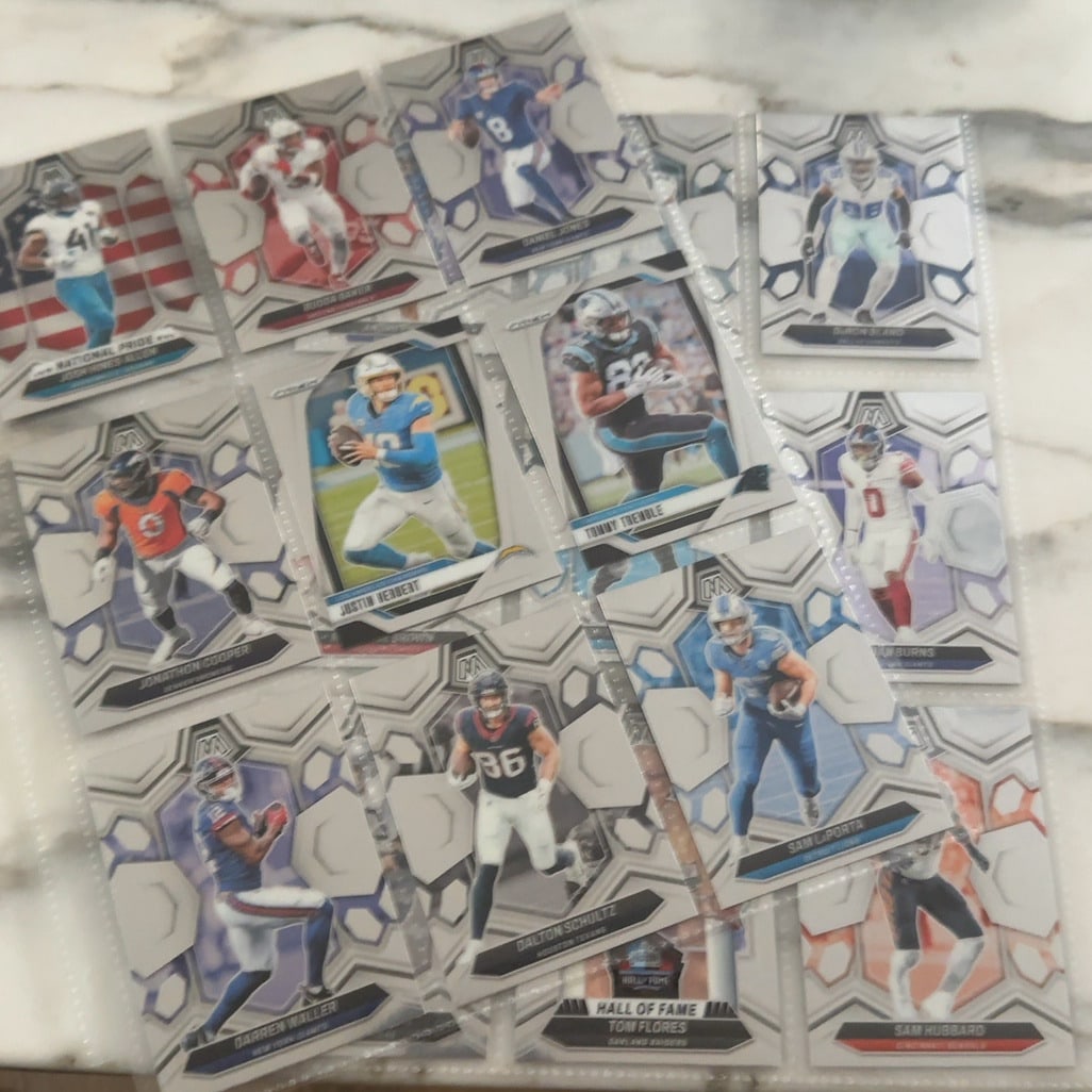 2023 Panini Mosaic Football Cards Assortment: This image displays a collection of various 2023 Panini Mosaic NFL football trading cards housed in protective plastic sleeves. The cards feature a signature geometric silver border design with