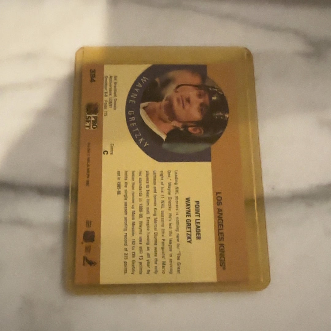 1991 Pro Set Wayne Gretzky Point Leader Card: This is a 1991 Pro Set hockey card featuring Los Angeles Kings legend Wayne Gretzky. The card highlights his status as a point leader and is preserved in a protective plastic top-loader.