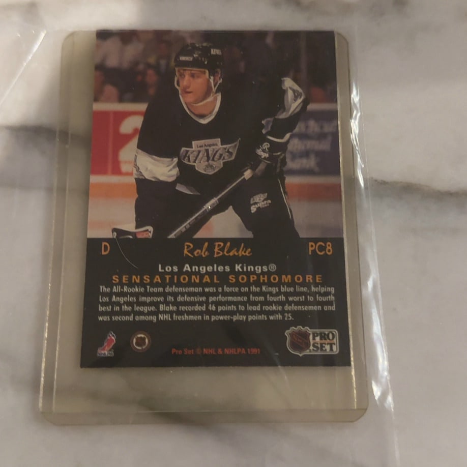 1991 Pro Set Sensational Sophomore Rob Blake Card: This is a 1991 Pro Set Sensational Sophomore hockey card featuring Rob Blake of the Los Angeles Kings. The card highlights his impressive rookie season performance and is preserved in a protective pla