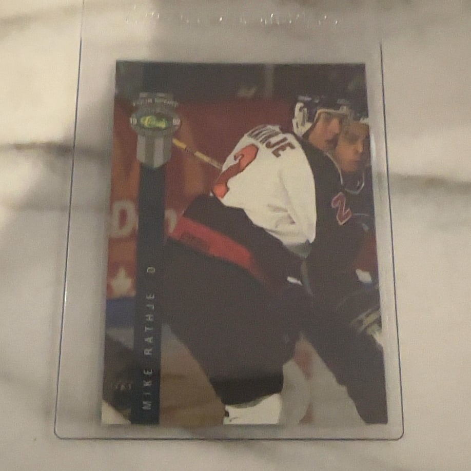 1992-93 Pinnacle Mike Rathje Hockey Card: This is a 1992-93 Pinnacle trading card featuring NHL player Mike Rathje. The card is preserved in a protective plastic top loader and showcases action photography from his early career.