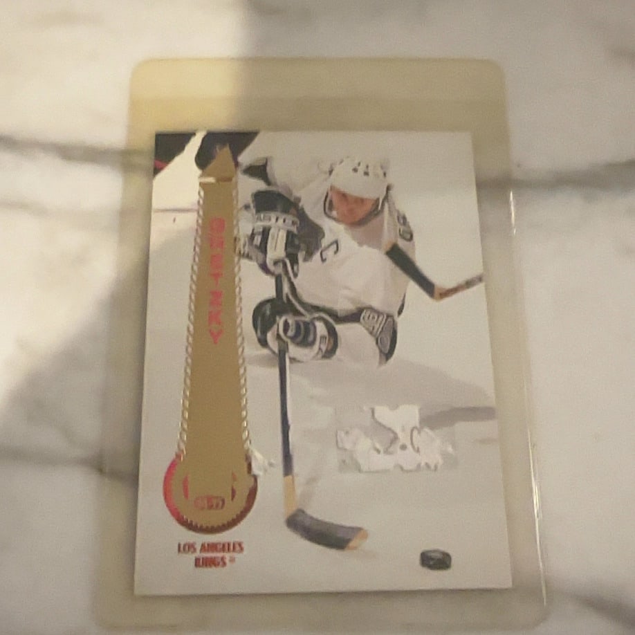 Wayne Gretzky 1996-97 Pinnacle Mint Collection Card: This is a 1996-97 Pinnacle Mint hockey trading card featuring NHL legend Wayne Gretzky. The card design incorporates a distinctive brass-colored token insert alongside an action shot of Gretzky in his