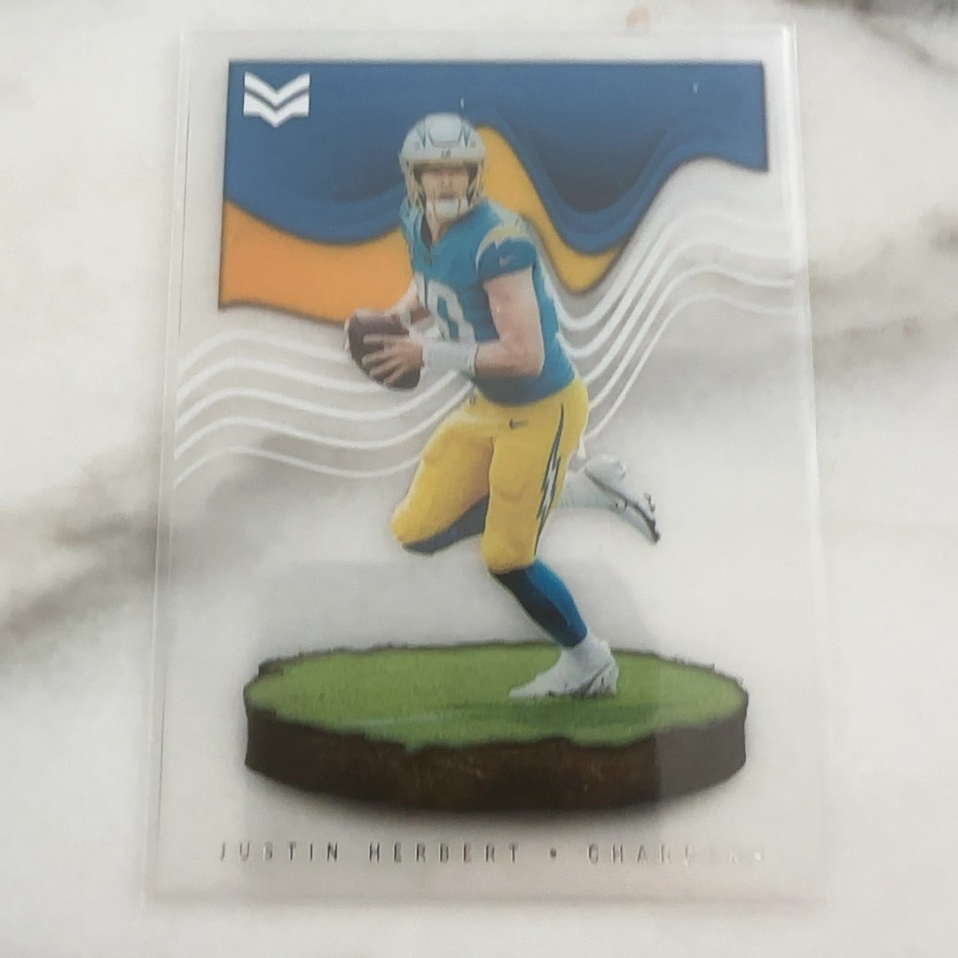 Football Trading Card: This is a trading card featuring Justin Herbert of the Los Angeles Chargers. The card is from the 2020 Panini Chronicles Momentum set, which utilizes a clear acetate design with a player action shot