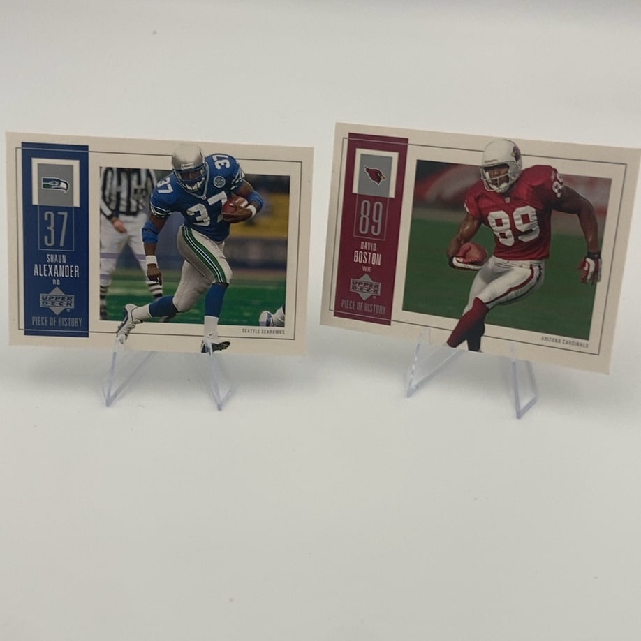 Shaun Alexander and David Boston Upper Deck Cards: This image shows two Upper Deck Piece of History football cards displayed on stands. One card features Seattle Seahawks running back Shaun Alexander, while the other features Arizona Cardinals wide
