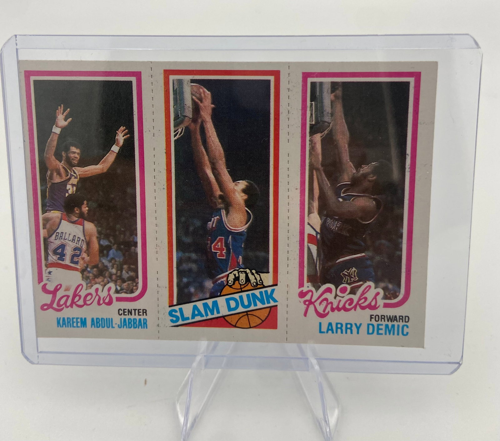 1980-81 Topps Basketball Kareem Abdul-Jabbar Slam Dunk Card: This is a 1980-81 Topps basketball card featuring a three-panel design. It displays Kareem Abdul-Jabbar, a Slam Dunk panel, and Larry Demic of the New York Knicks. The card is preserved in a hard