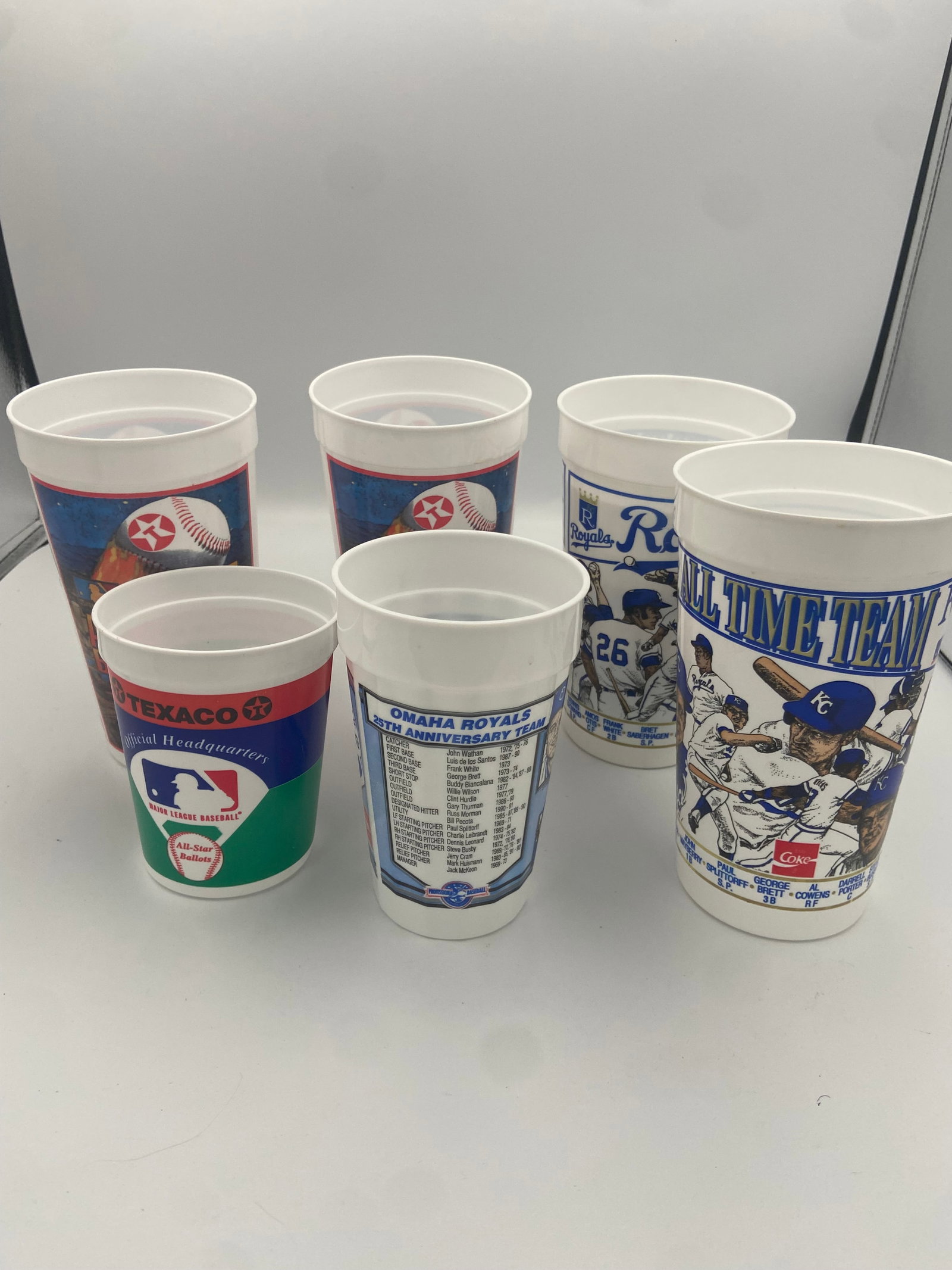 Kansas City Royals Commemorative Promotional Cups: This set includes vintage plastic cups featuring Kansas City Royals themes, including an All-Time Team edition and an Omaha Royals 25th Anniversary edition. The cups serve as historical baseball memor