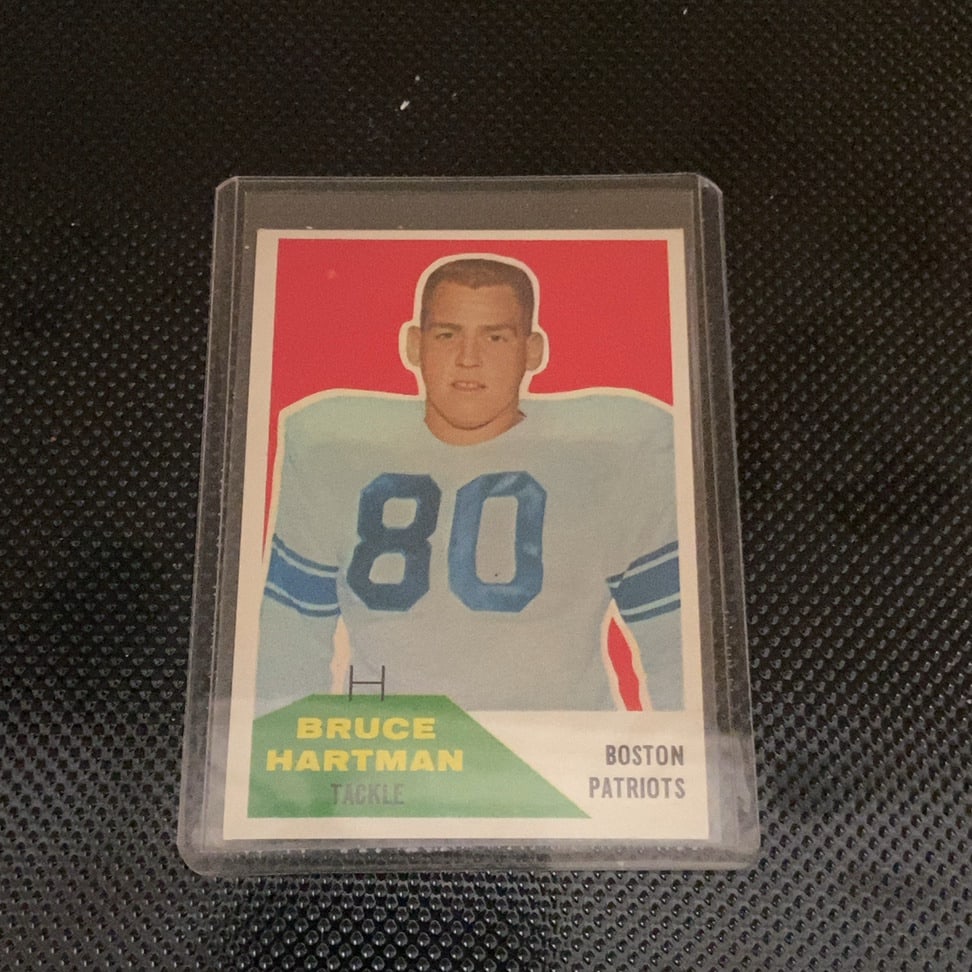 1960 Topps Bruce Hartman Boston Patriots Football Card: This is a 1960 Topps football trading card featuring Bruce Hartman of the Boston Patriots. The card is encased in a protective plastic sleeve and shows the player's portrait against a red background