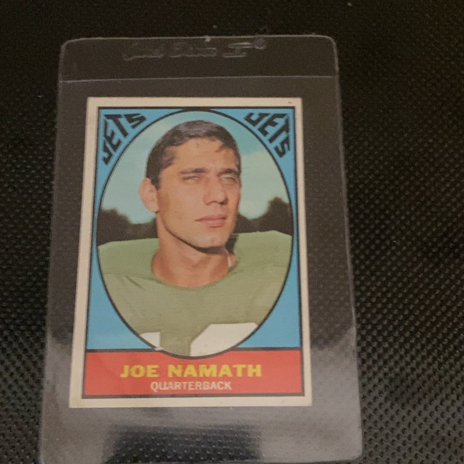 1968 Topps Joe Namath New York Jets Trading Card: This is a 1968 Topps Joe Namath New York Jets trading card. It features the iconic Hall of Fame quarterback in his classic green jersey. The card is encased in a protective plastic sleeve and appears