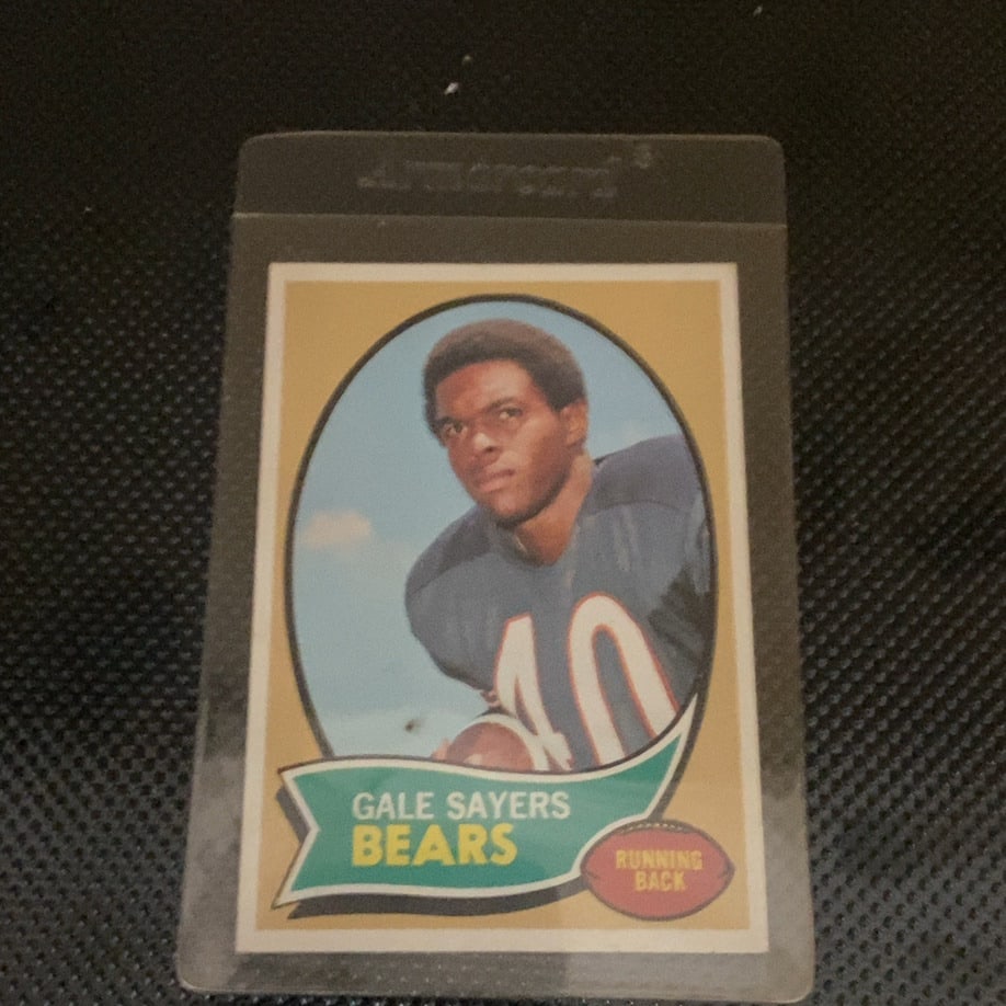 1970 Topps Gale Sayers Chicago Bears Football Card: This is a 1970 Topps football card featuring Chicago Bears running back Gale Sayers. The card showcases a classic portrait-style design with a team-colored banner and position label. It is protected