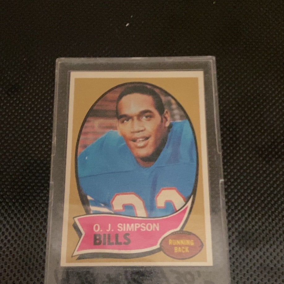 1970 Topps O.J. Simpson Rookie Card: This is a 1970 Topps O.J. Simpson rookie card featuring the Buffalo Bills running back. The card is preserved in a hard plastic protective case. It showcases the classic design from the 1970 football