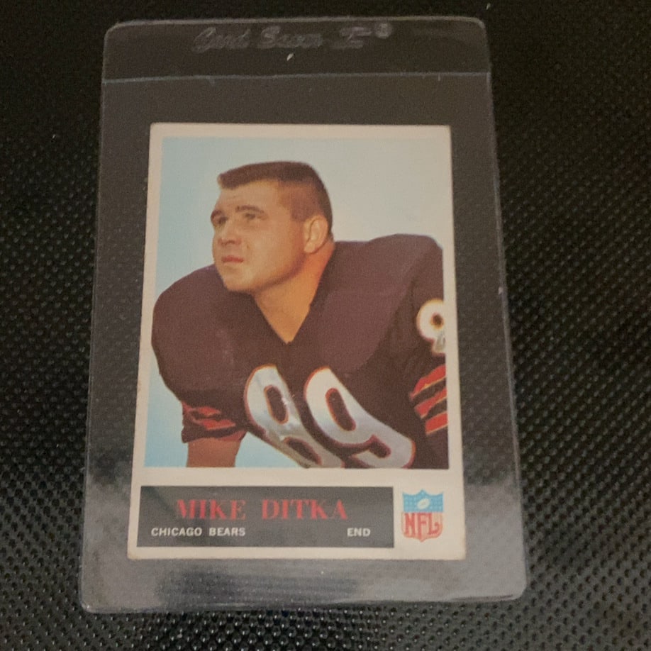 Vintage Mike Ditka Chicago Bears Football Card: This is a vintage football card featuring Mike Ditka of the Chicago Bears. The card displays his name, team, position, and the official NFL logo. It is protected within a clear plastic top loader