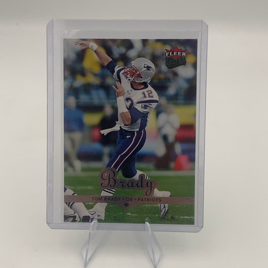 Tom Brady Fleer Ultra Football Card: This is a 2002 Fleer Ultra football trading card featuring New England Patriots quarterback Tom Brady. The card displays a dynamic action shot of Brady in his team uniform and is protected in a clear