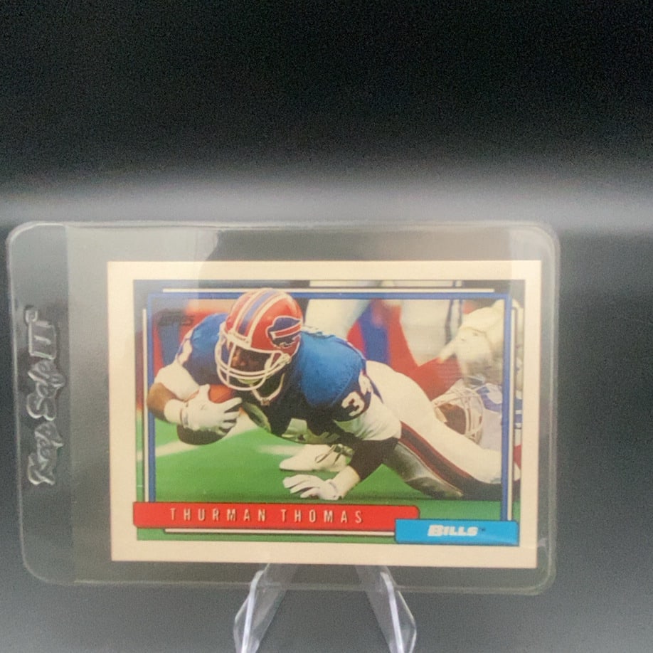 Thurman Thomas Topps Football Card: This is a Topps trading card featuring Buffalo Bills running back Thurman Thomas in action. The card shows Thomas in his team uniform with the Bills logo displayed prominently. The card is encased in