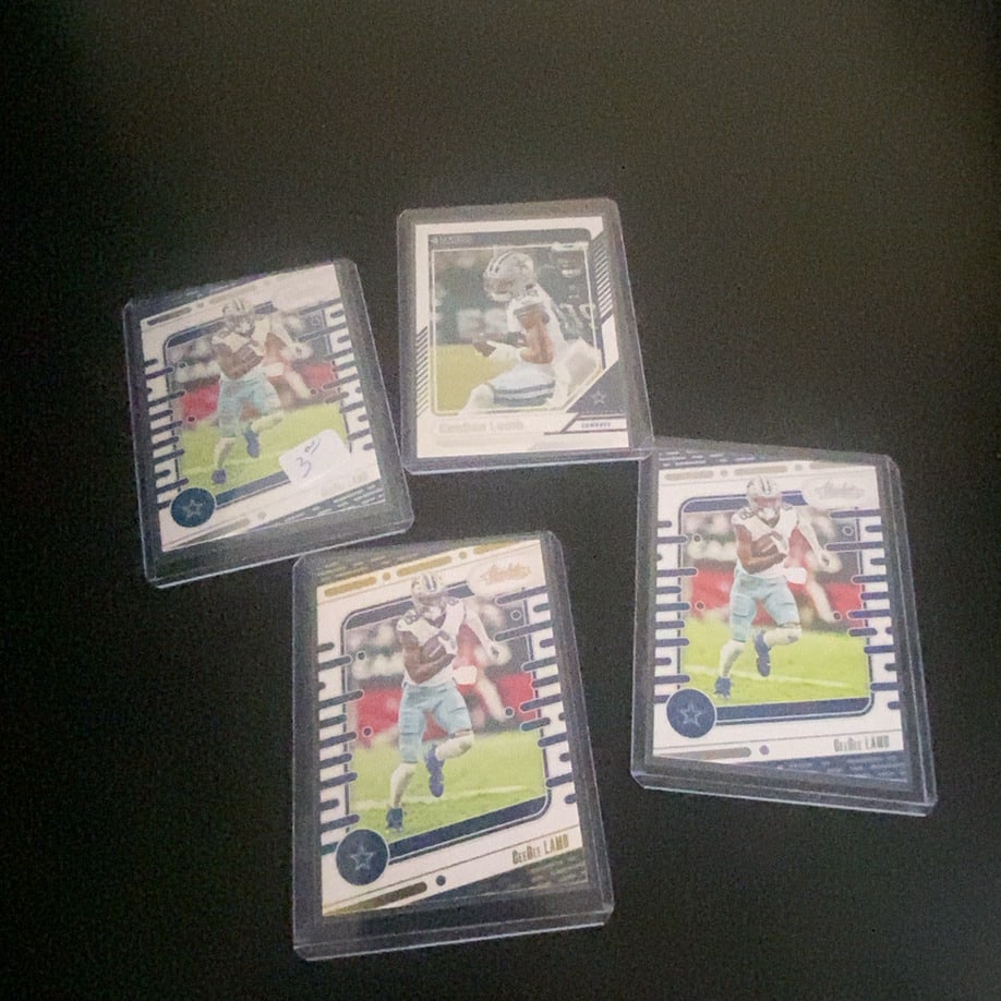 CeeDee Lamb Absolute Football Cards: This image features four CeeDee Lamb trading cards from the Panini Absolute Football set. The cards are encased in protective top-loaders and show the Dallas Cowboys player in his game uniform. One