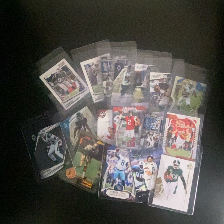 Assorted Football Trading Cards: This is a collection of various football trading cards in protective sleeves. Brands visible include Prestige, Score, and others, featuring different players and team gear. The cards appear to be a