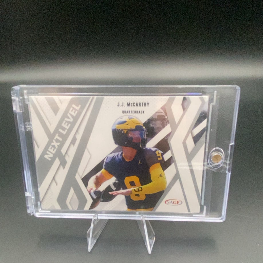 J.J. McCarthy Next Level: This is a trading card featuring J.J. McCarthy in his University of Michigan uniform, positioned as a Quarterback. The card is labeled 'NEXT LEVEL' and was produced by SAGE. It is encased in a