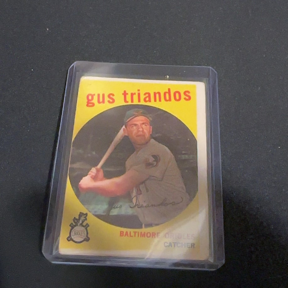 1961 Topps Gus Triandos Baltimore Orioles Baseball Card: This is a 1961 Topps baseball card featuring Gus Triandos of the Baltimore Orioles. The card shows Triandos in a batting pose and is preserved in a protective hard plastic case, appearing to be in goo