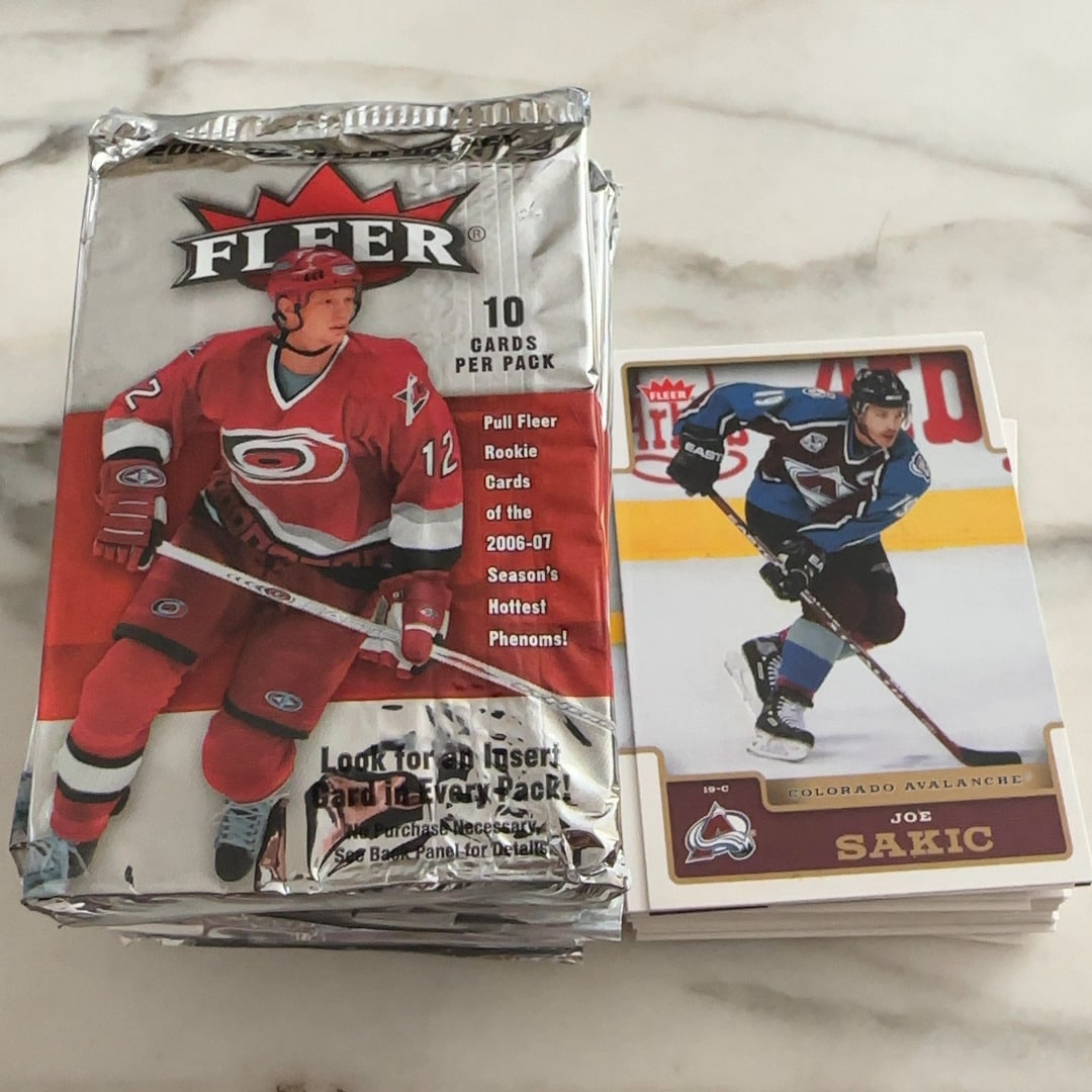 2006-07 Fleer Joe Sakic: This item features a sealed pack of 2006-07 Fleer hockey cards alongside a Joe Sakic card from the Colorado Avalanche. The packaging highlights the inclusion of rookie cards for the 2006-07 season and