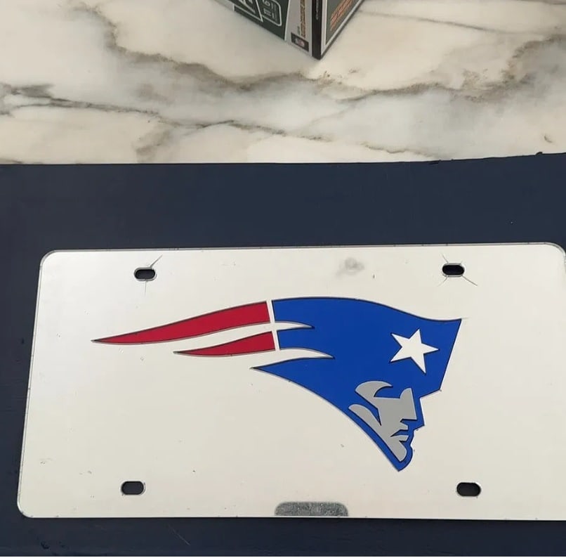 New England Patriots License Plate: license plate featuring the official logo of the New England Patriots NFL team. The plate displays the classic Patriot logo against a white background, complete with mounting holes.