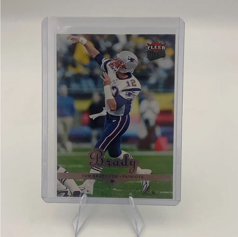 Tom Brady Fleer Ultra Football Card: This is a 2002 Fleer Ultra football trading card featuring New England Patriots quarterback Tom Brady. The card displays a dynamic action shot of Brady in his team uniform and is protected in a clear
