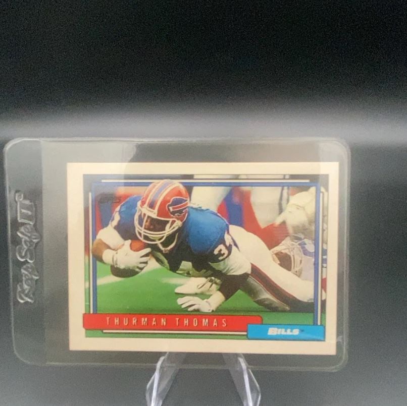 Thurman Thomas Topps Football Card: This is a Topps trading card featuring Buffalo Bills running back Thurman Thomas in action. The card shows Thomas in his team uniform with the Bills logo displayed prominently. The card is encased in 