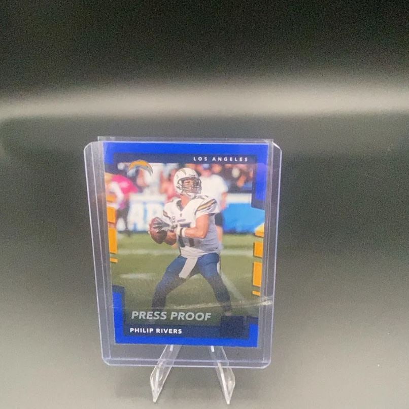 Philip Rivers Press Proof Card: This is a collectible trading card featuring Philip Rivers of the Los Angeles Chargers. The card is labeled as a 'Press Proof' version and is housed in a protective plastic sleeve.