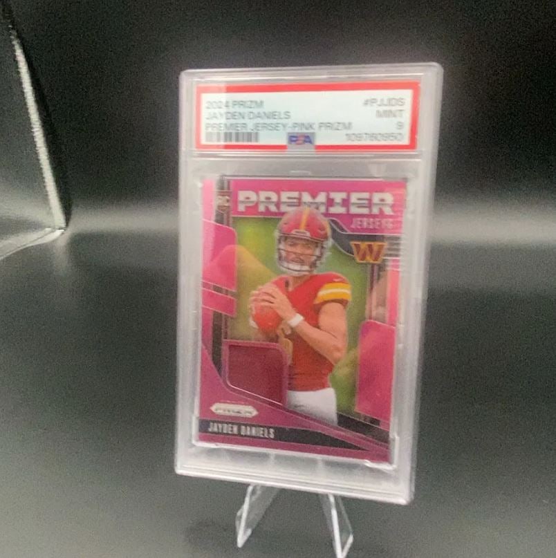 2024 Prizm Jayden Daniels Premier Jersey Pink Prizm: This is a 2024 Panini Prizm football card featuring Jayden Daniels in a Premier Jersey Pink Prizm parallel. The card is professionally graded by PSA and holds a Mint 9 grade. It includes a visible