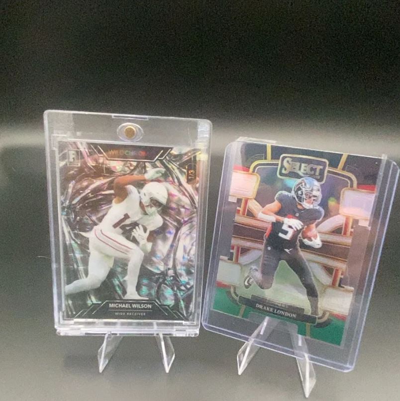 2023 Wild Card Michael Wilson and 2022 Panini Select Drake L: This image features two football trading cards protected in plastic cases. One card depicts wide receiver Michael Wilson from the 2023 Wild Card set, while the other shows wide receiver Drake London