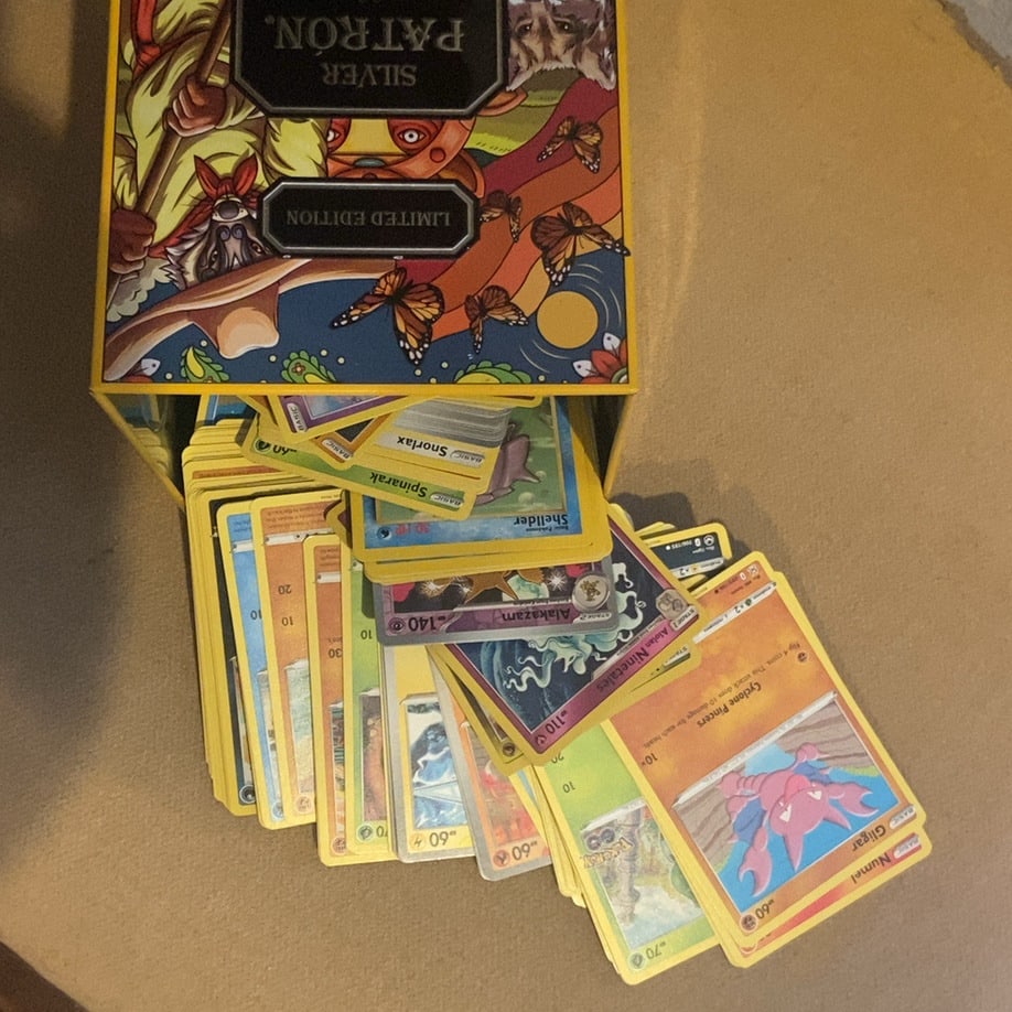 Pokémon Trading Card Collection with Storage Box: This lot features a collection of assorted Pokémon trading cards housed in a yellow decorative storage box. Visible cards include Gligar and Numel, and the set appears to include various generati