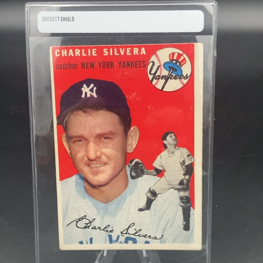 1954 Topps Charlie Silvera (#96) baseball card: This is a vintage trading card featuring Charlie Silvera, a catcher for the New York Yankees. The card features a portrait of the player alongside an action illustration and the Yankees team logo.