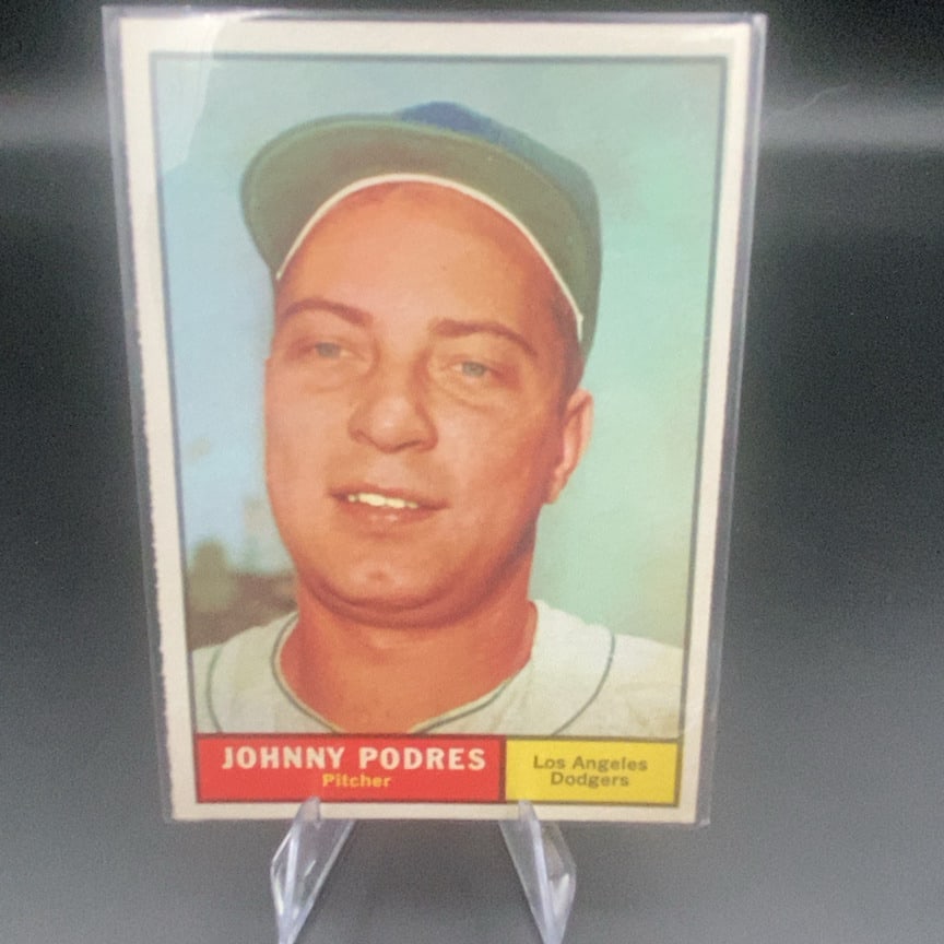 1961 Topps #109 Johnny Podres baseball trading card: This is a vintage baseball card featuring Johnny Podres, a pitcher for the Los Angeles Dodgers. The card is protected in a clear plastic sleeve and displayed on a stand. It features a portrait of the