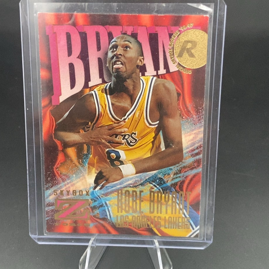 1996-97 SkyBox Z-Force Kobe Bryant Rookie Card: This is a 1996-97 SkyBox Z-Force rookie card featuring NBA legend Kobe Bryant. It is encased in a protective plastic top loader. The card showcases the classic design and the distinctive 'Official