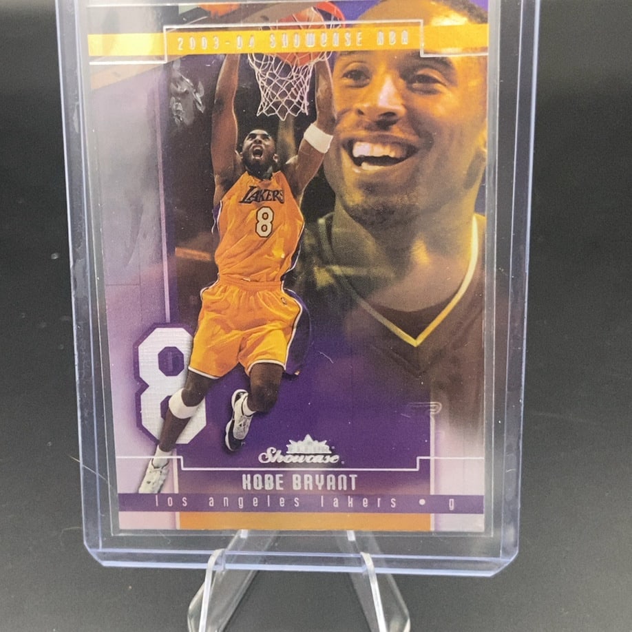 2003-04 Fleer Showcase Kobe Bryant: This is a 2003-04 Fleer Showcase basketball card featuring Kobe Bryant of the Los Angeles Lakers. The card captures him in an iconic dunking pose with a large portrait of him in the background. It is