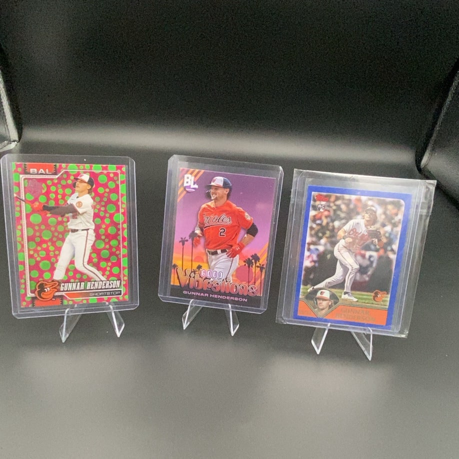 Gunnar Henderson Orioles Trading Card Collection: This lot features three separate Gunnar Henderson baseball cards, all showcasing the Baltimore Orioles shortstop. The cards feature various designs, including a vibrant neon green pattern, a