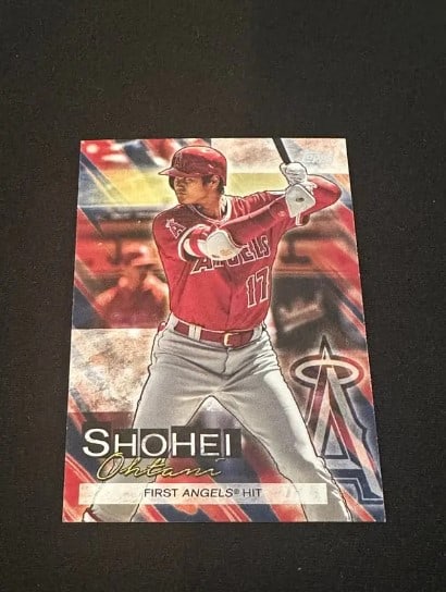 Topps Shohei Ohtani First Angels Hit: This is a Topps baseball card featuring Shohei Ohtani in his Los Angeles Angels uniform. The card commemorates his First Angels Hit. It features a dynamic action shot of Ohtani at bat with the team