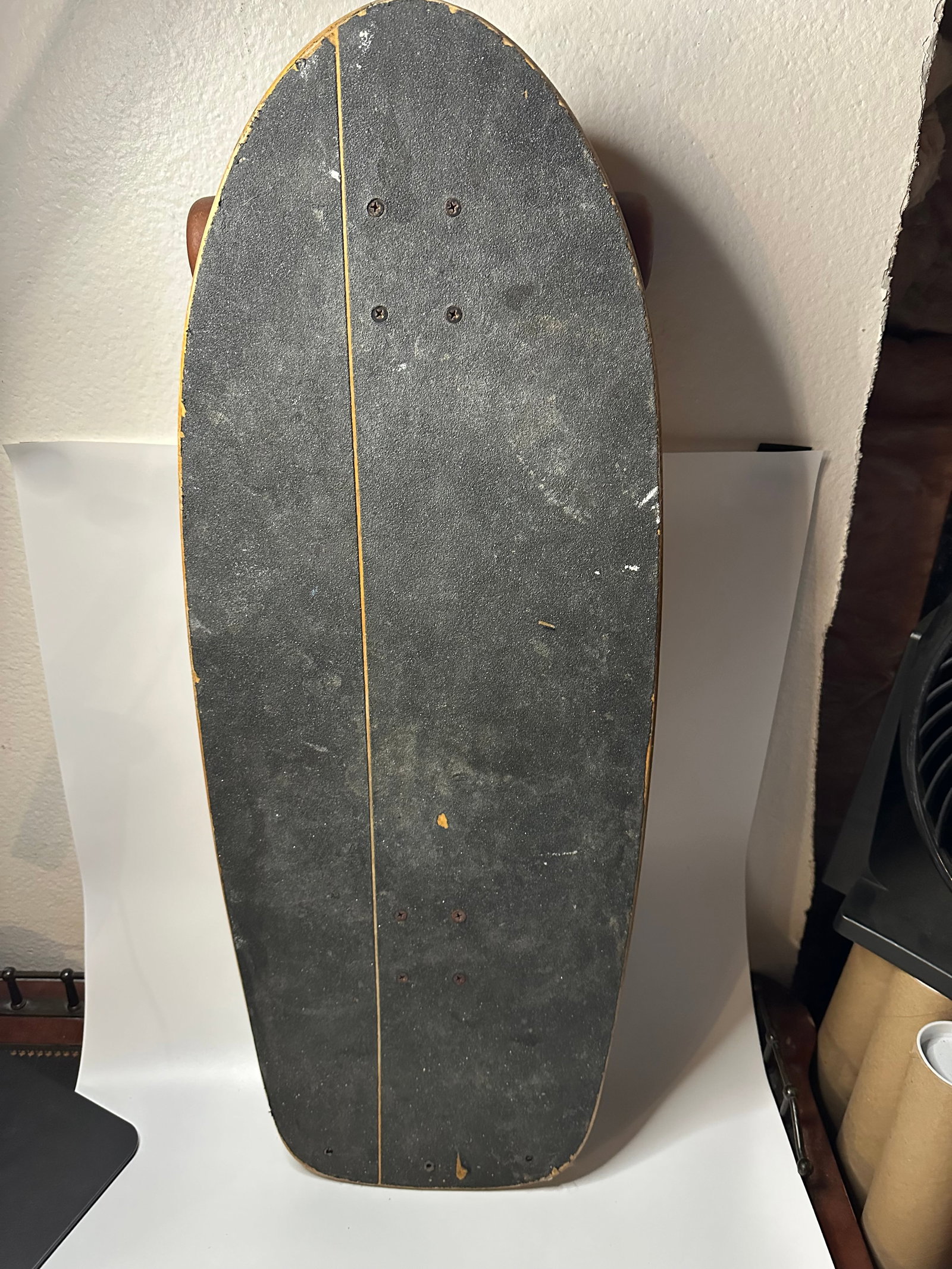 Vintage Skateboard: This is a top-down view of a vintage wooden skateboard with a black grip tape surface. The deck features a horizontal line detail and clear signs of use consistent with its age.